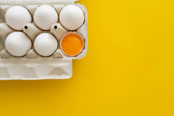 Dotter in der Schale neben Eiern in Karton auf gelbem Hintergrund — Stockfoto
