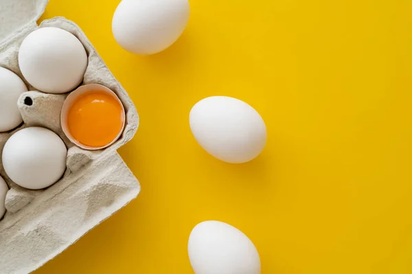 Vista superior de los huevos cerca de la yema fresca en cáscara en contenedor sobre fondo amarillo - foto de stock