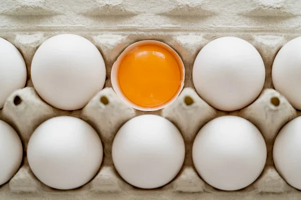Top view of fresh yolk in shell near white eggs in cardboard tray — Stock Photo