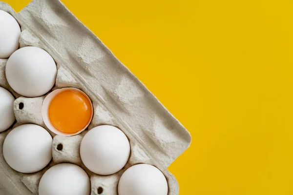 Top view of natural yolk in shell near eggs in carton box isolated on yellow — Stock Photo