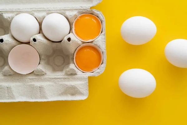 Top view of natural yolks near eggs in container on yellow background — Stock Photo