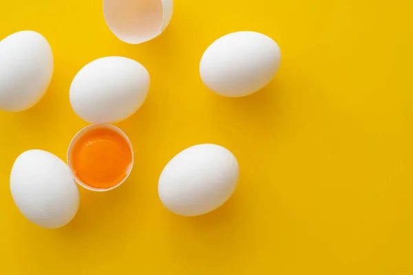 Top view of natural yolk in shell near eggs on yellow background — Stock Photo
