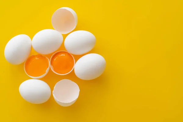 Vista superior de huevos y yemas en cáscaras sobre fondo amarillo - foto de stock