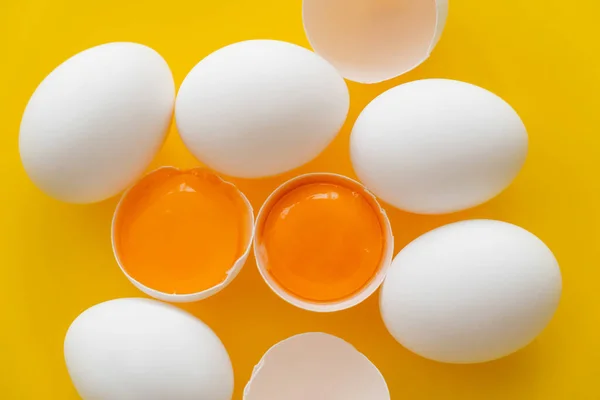 Top view of organic yolks in shells and white eggs on yellow background — Stock Photo