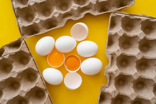 Top view of eggs and raw yolks near carton trays on yellow background — Stock Photo