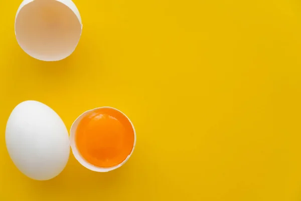 Top view of natural yolk in shell near white egg on yellow background — Stock Photo