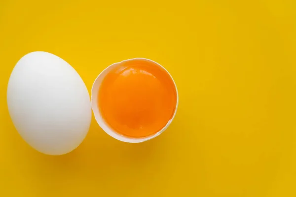 Top view of white egg near raw yolk in shell on yellow background — Stock Photo