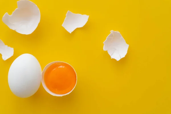 Draufsicht auf Eigelb in der Nähe von rissigen Schalen und Eiern auf gelbem Hintergrund — Stockfoto