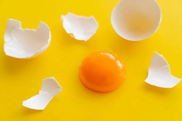 Close up view of raw yolk near cracked egg shell on yellow background — Stock Photo