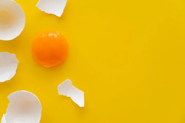 Vista superior de la yema natural y cáscara de huevo agrietada sobre fondo amarillo - foto de stock