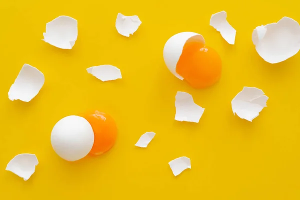 Top view of natural yolks and cracked egg shells on yellow background — Stock Photo