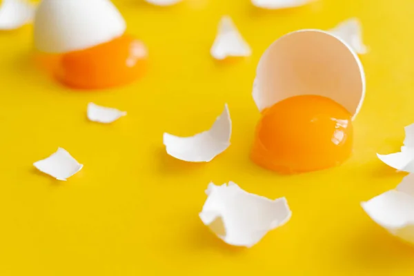 Close up view of fresh yolk and cracked egg shells on yellow surface — Stock Photo