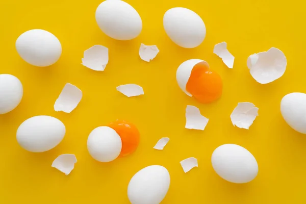 Top view of eggs near yolks and cracked shells on yellow background — Stock Photo