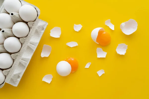 Vista superior de yemas crudas y cáscaras agrietadas cerca de huevos en bandeja sobre fondo amarillo - foto de stock