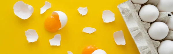 Top view of natural yolks and shells near eggs in carton tray on yellow background, banner — Stock Photo