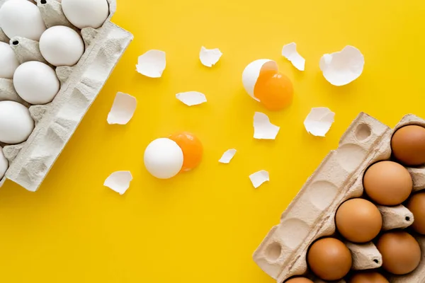 Top view of fresh yolks and shells near eggs in containers on yellow background — Stock Photo