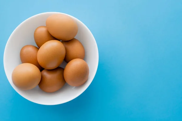 Vue du dessus des œufs de poulet dans un bol sur fond bleu — Photo de stock