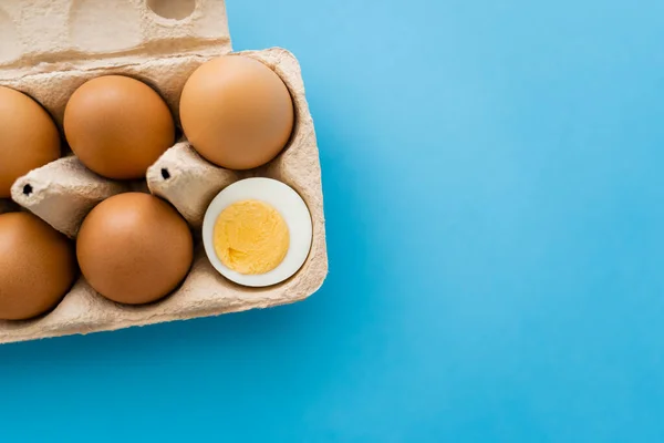 Top view of cut boiled and raw egg in carton tray on blue background — Stock Photo