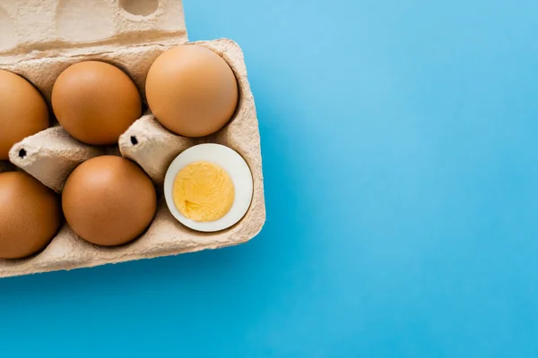 Vue du dessus de l'oeuf cuit et cru coupé dans un bac en carton sur fond bleu — Photo de stock