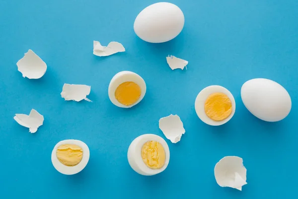 Vue du dessus des œufs durs avec jaunes près des coquilles fissurées sur fond bleu — Photo de stock