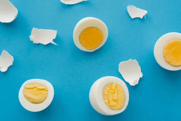 Top view of cut boiled eggs and shells on blue surface — Stock Photo