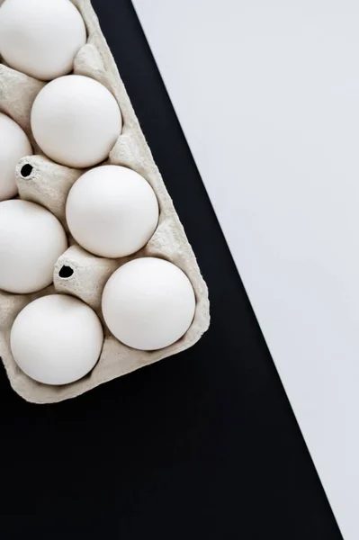 Vue du dessus des œufs de poulet frais dans un récipient en carton sur fond blanc et noir — Photo de stock