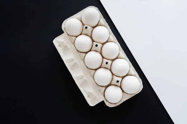 Top view of fresh chicken eggs in tray on white and black surface — Stock Photo