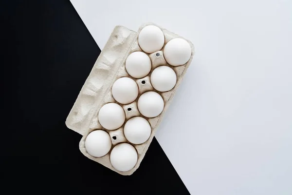 Top view of fresh organic eggs in cardboard tray on white and black surface — Stock Photo