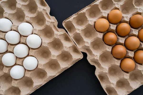 Vue du dessus des œufs de poulet blancs et bruns dans un plateau en carton sur fond noir — Photo de stock