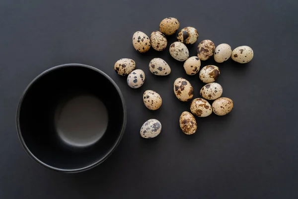 Top view of natural quail eggs near bowl on black background — Stock Photo