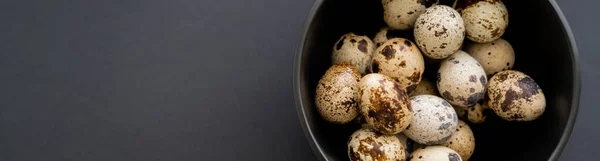 Top view of natural quail eggs in bowl on black surface, banner — Stock Photo