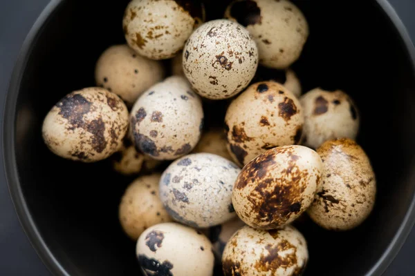 Close up view of fresh perail eggs in bowl on black background — стоковое фото