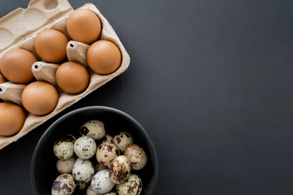 Vue du dessus des oeufs de caille et de poulet dans un bol et un plateau sur fond noir — Photo de stock