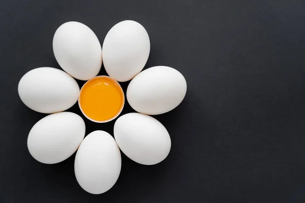 Puesta plana de yema cruda en cáscara cerca de huevos de pollo sobre fondo negro - foto de stock