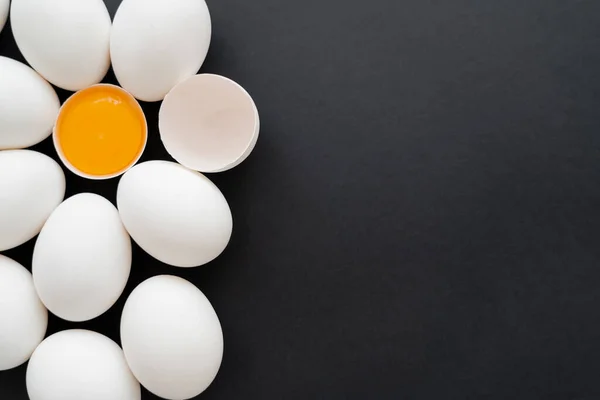 Vue du dessus des œufs de poulet blancs près du jaune cru en coquille sur une surface noire — Photo de stock