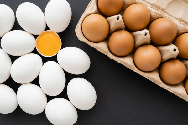 Vista superior de ovos de galinha marrom e branco perto de bandeja de papelão em fundo preto — Fotografia de Stock