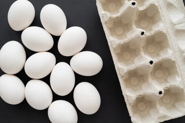 Draufsicht auf Karton-Tablett und weiße Eier auf schwarzem Hintergrund — Stockfoto