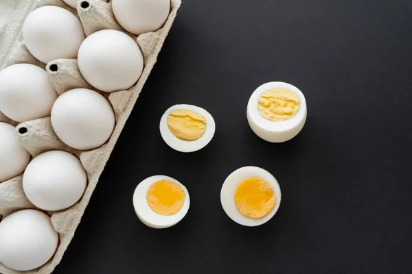 Top view of boiled and raw eggs in cardboard container on black surface — Stock Photo