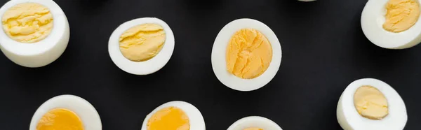 Top view of cut boiled eggs with yolks on black background, banner — Stock Photo