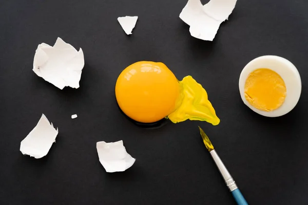 Top view of paintbrush near raw yolk and egg shell on black background — Stock Photo