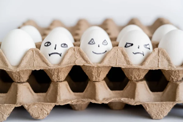 Huevos pintados con diferentes expresiones faciales en cajas de cartón sobre fondo blanco - foto de stock