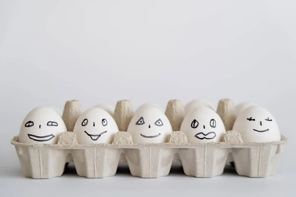 Huevos de pollo pintados con expresiones faciales en bandeja sobre fondo blanco - foto de stock