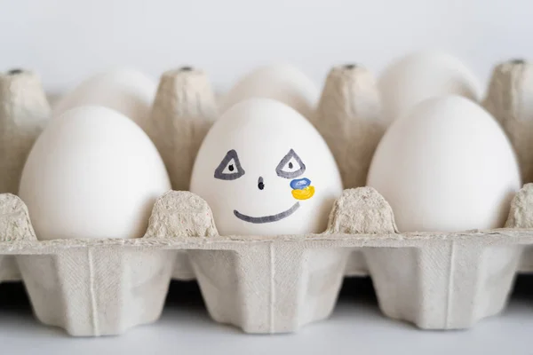 Bemaltes Ei mit Gesichtsausdruck und ukrainischer Flagge auf weißem Hintergrund — Stockfoto