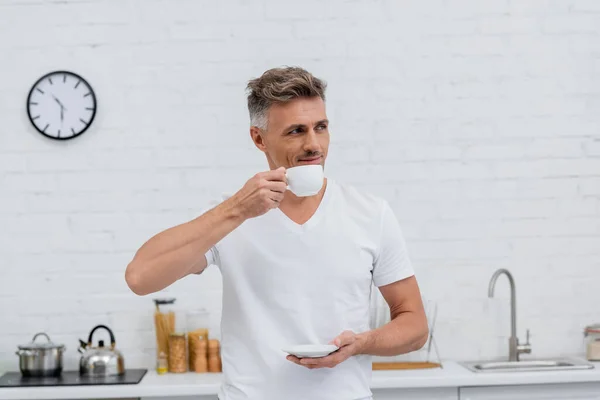 Man in t-shirt holding cup of coffee in kitchen in morning — Stock Photo