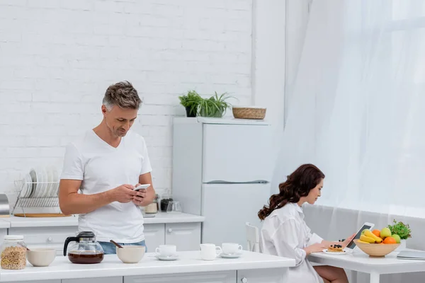 Couple using devices near breakfast and coffee in kitchen — Stock Photo