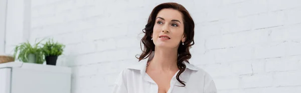 Brunette woman in shirt looking away in kitchen, banner — Stock Photo