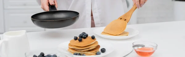 Cropped view of woman in shirt putting pancake on plate near fresh blueberries in kitchen, banner — Stock Photo