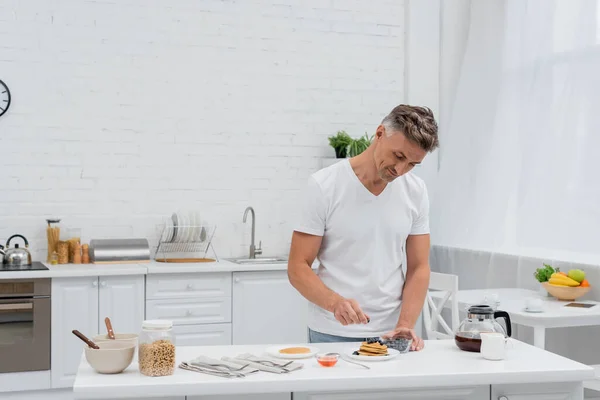 Man holding blueberries near delicious pancakes and coffee in kitchen — Stock Photo