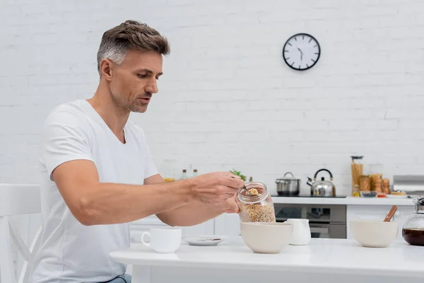 Homme tenant petit déjeuner céréalier près des bols et café dans la cuisine — Photo de stock