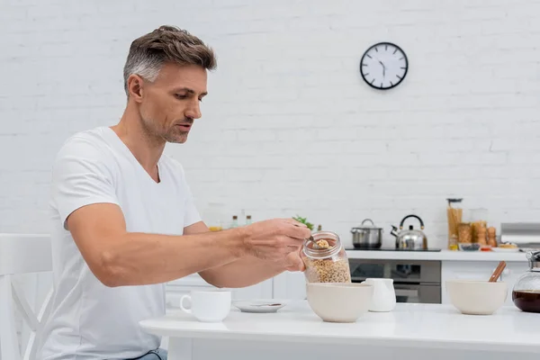 Homem segurando café da manhã de cereais perto de tigelas e café na cozinha — Fotografia de Stock